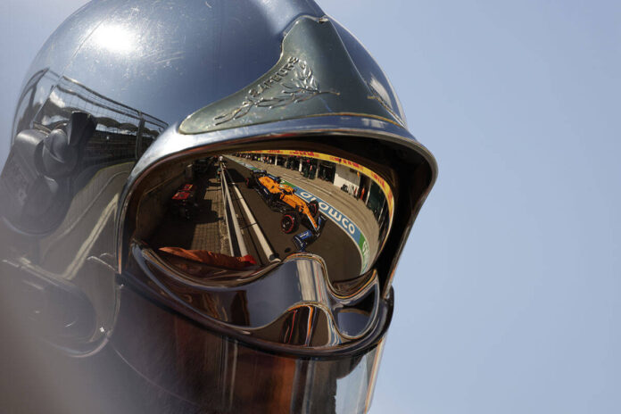 Daniel Ricciardo, McLaren MCL35M, reflected in a fire marshals helmet